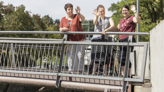 zwei Klientinnen und eine Betreuerin von Viv Riva in Rapperswil-Jona winken fröhlich von einer Brücke