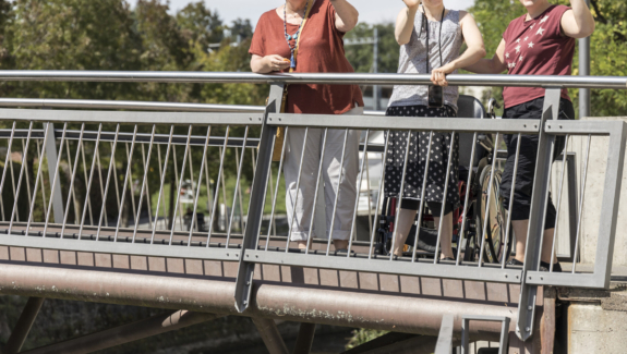 zwei Klientinnen und eine Betreuerin von Viv Riva in Rapperswil-Jona winken fröhlich von einer Brücke