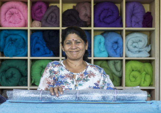Eine Klientin sitzt im Textilatelier vor einem Holzregal mit bunten Stoffrollen